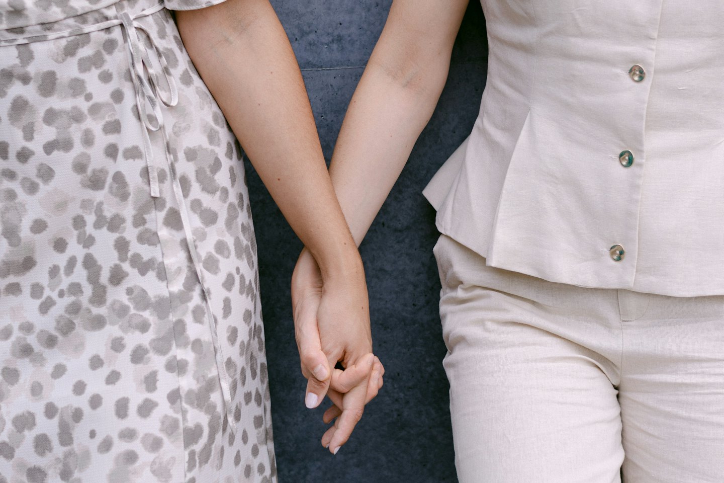 Two people hold hands while standing against a concrete wall.
